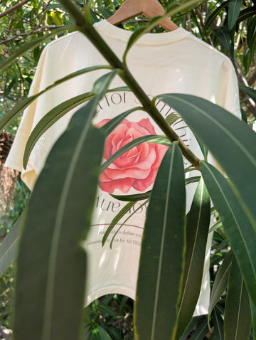 White t-shirt with pink rose design hanging among green leaves